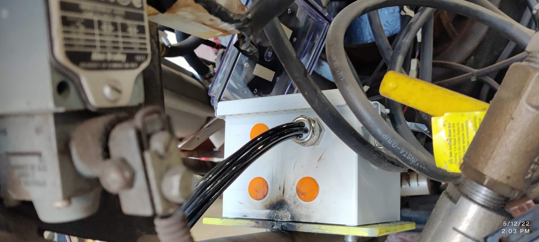 Field enclosure mounted onto a welding machine with a cable gland carrying sensor leads, hydraulic lines packed around it
